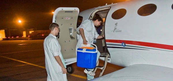 Personnel médical embarquant dans un avion Luxembourg Air Rescue de nuit avec une glacière de transport d’organes pour une mission urgente.