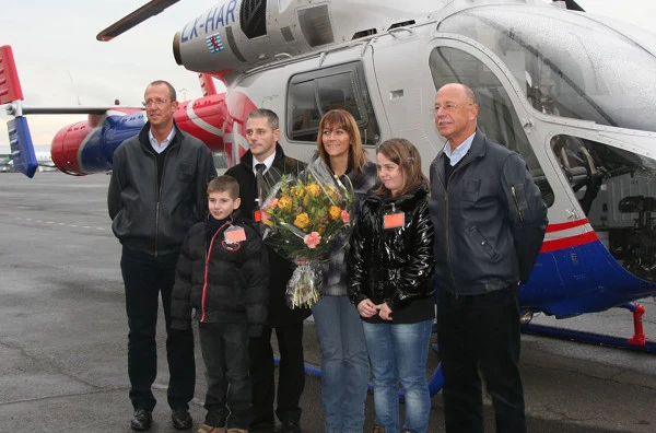 Équipage Luxembourg Air Rescue avec une famille secourue et des fleurs, illustrant l’aide humanitaire et les soins aux patients.