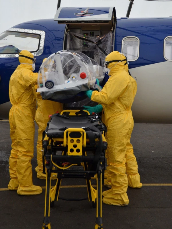 Équipe médicale en combinaison de protection chargeant une unité d’isolement dans un avion Luxembourg Air Rescue pour transport de patients infectieux.
