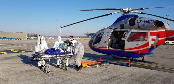 Équipe médicale Luxembourg Air Rescue en combinaison de protection préparant un transfert de patient en hélicoptère durant la pandémie COVID-19.