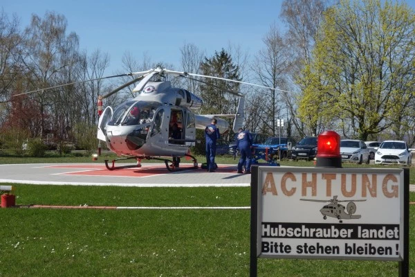 Hélicoptère Luxembourg Air Rescue atterrissant sur une hélisurface avec panneau « Achtung Hubschrauber landet », intervention en cours.