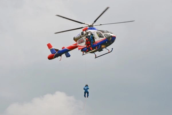 Hélicoptère Luxembourg Air Rescue effectuant une opération de treuillage avec une personne suspendue, démontrant ses capacités de secours.
