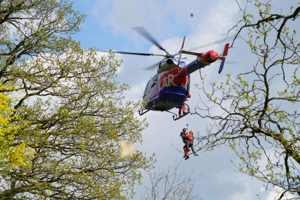 Hélicoptère Luxembourg Air Rescue effectuant un sauvetage par treuillage en zone forestière, illustrant les opérations de secours avancées.