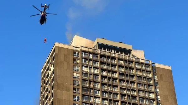 Hélicoptère Luxembourg Air Rescue effectuant un sauvetage par treuillage près d’un immeuble, illustrant les capacités urbaines de secours.