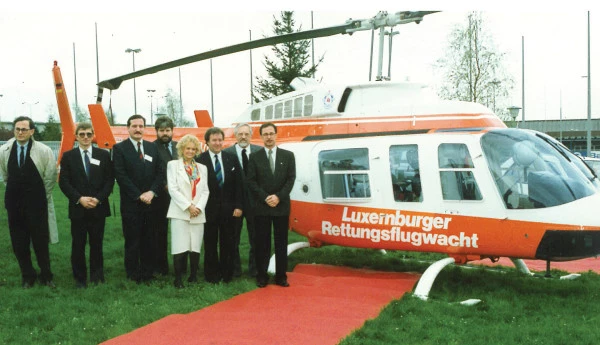 Groupe de responsables posant devant un hélicoptère de secours aérien luxembourgeois lors d’un événement officiel sur tapis rouge.