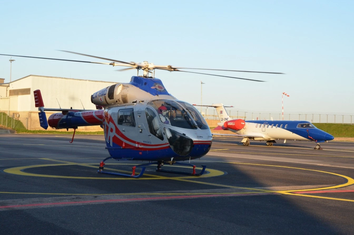 Rettungshubschrauber von Luxembourg Air Rescue auf dem Helipad mit Ambulanzflugzeug im Hintergrund am Flughafen Findel.