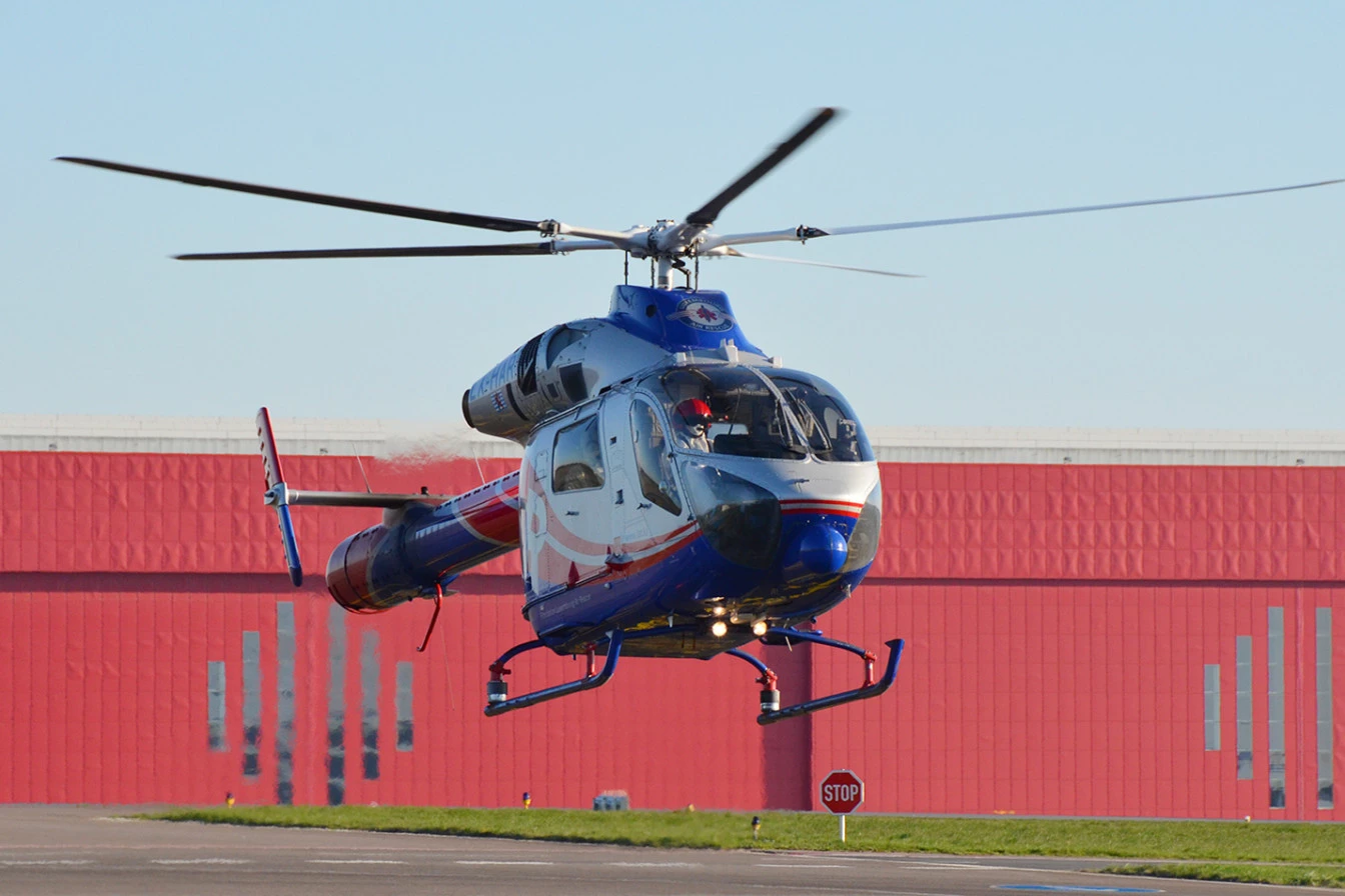 Hélicoptère Luxembourg Air Rescue en vol stationnaire au-dessus du tarmac lors d’une mission de sauvetage.