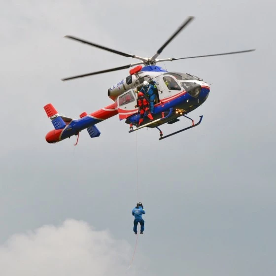Hélicoptère Luxembourg Air Rescue en opération de treuillage avec un secouriste suspendu lors d’une mission de sauvetage.