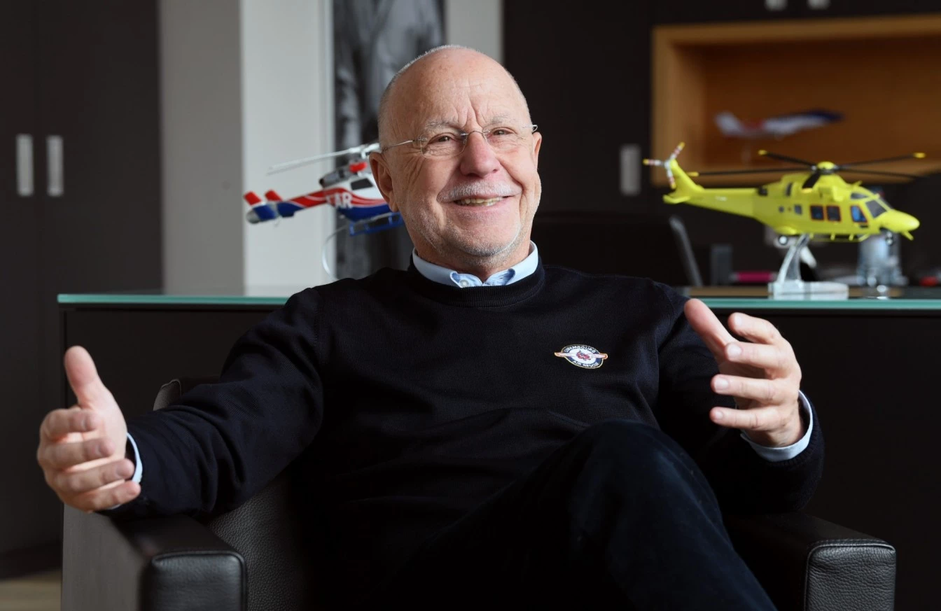 René Closter, founder of Luxembourg Air Rescue, sitting in an office in front of helicopter models while speaking.