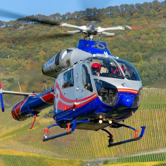 Luxembourg Air Rescue helicopter flying over vineyards with pilot visible in the cockpit.