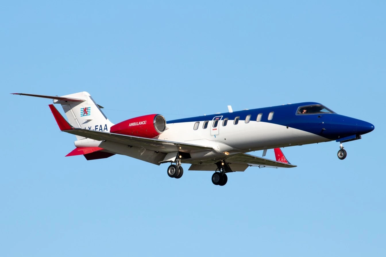 Luxembourg Air Rescue air ambulance aircraft in flight with landing gear deployed and “Ambulance” marking on the fuselage.