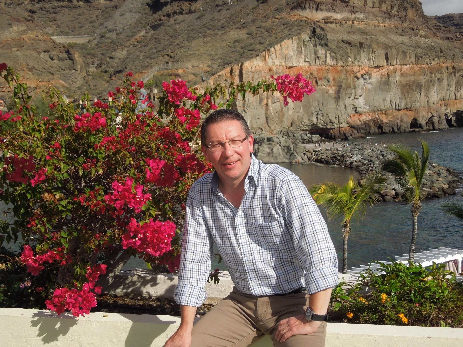 Homme posant en extérieur devant des falaises côtières et des fleurs.