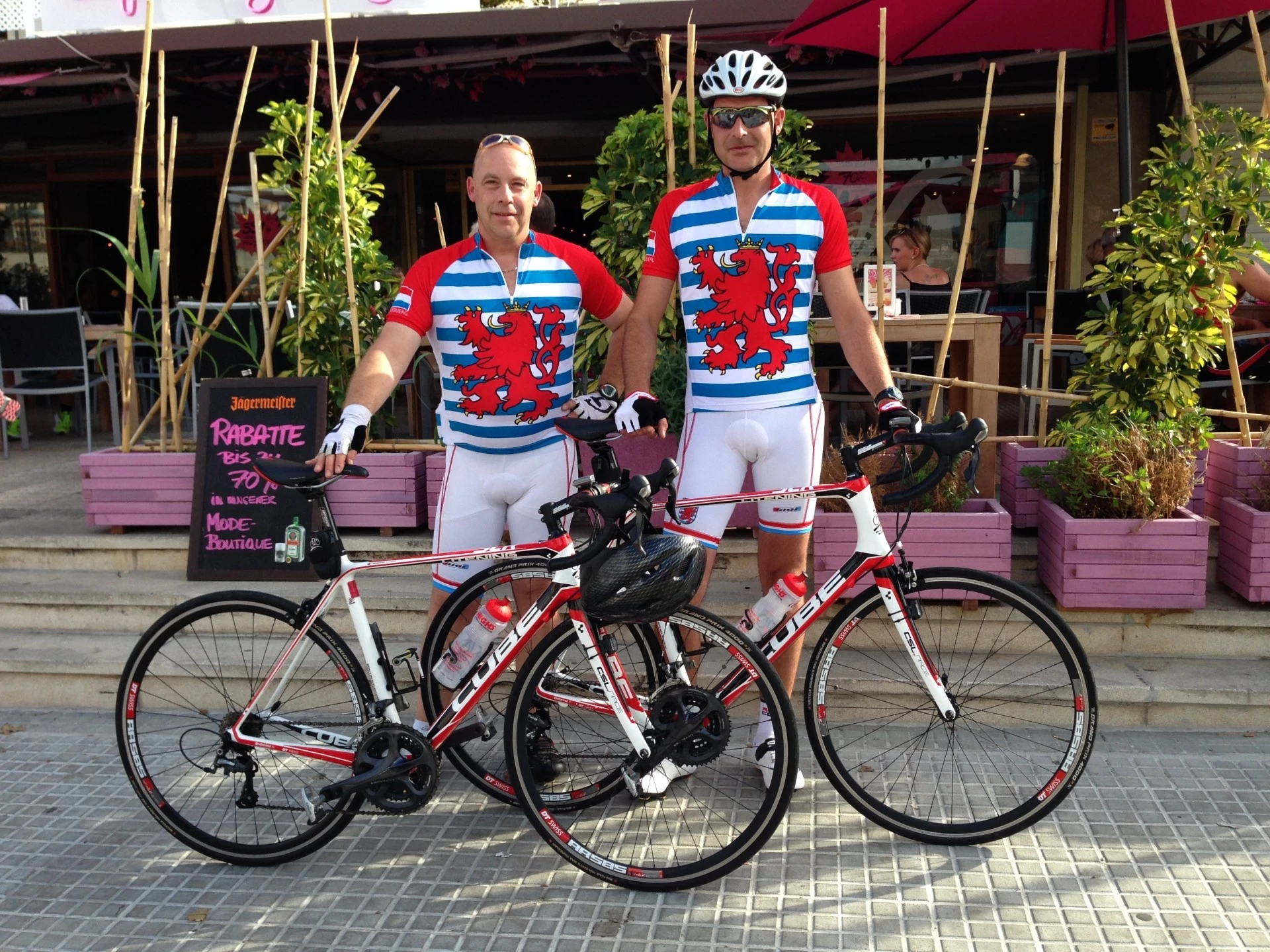 Deux cyclistes posant avec leurs vélos de route devant un café.
