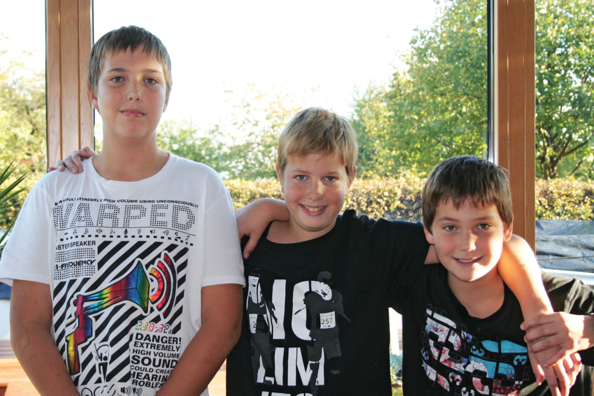 Trois enfants debout ensemble en intérieur près d’une grande fenêtre