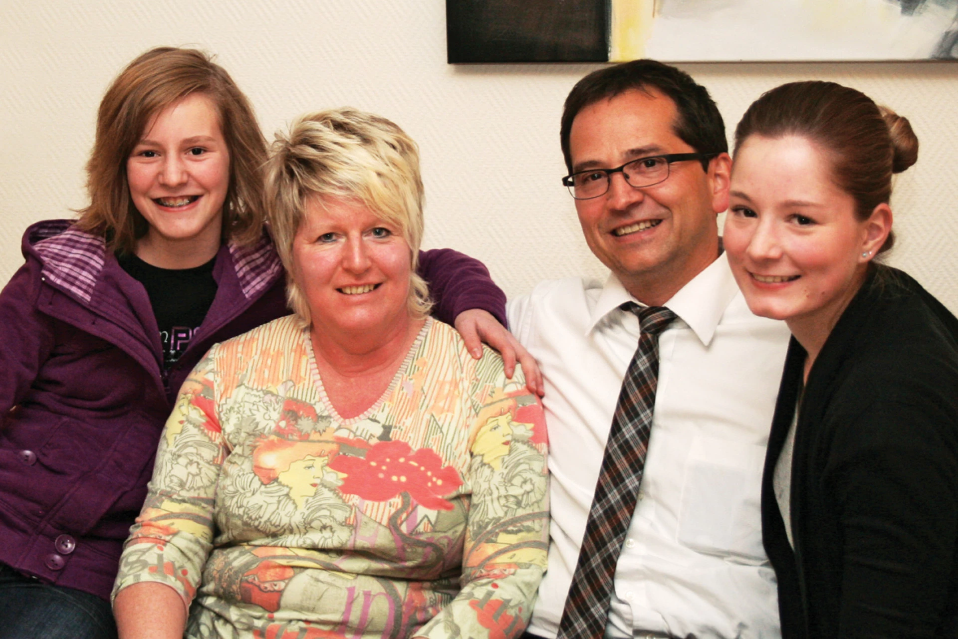 Vierköpfige Familie sitzt eng zusammen und lächelt