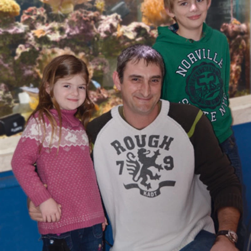 Man posing indoors with two children in front of an aquarium display