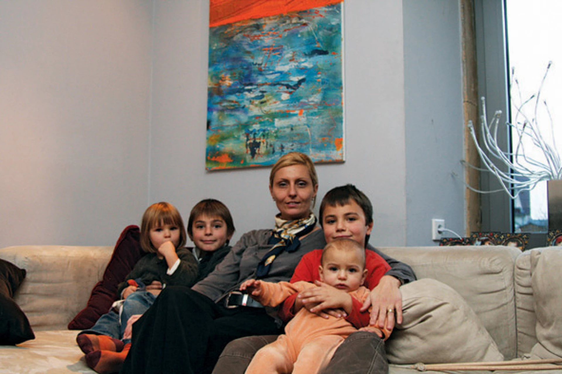 Frau sitzt mit mehreren Kindern auf einem Sofa in einem gemütlichen Wohnzimmer