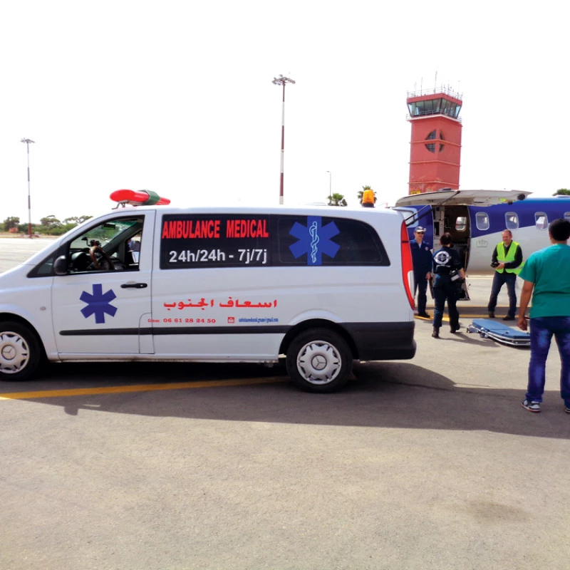 Medical ambulance on airport tarmac next to a small aircraft during patient transfer.