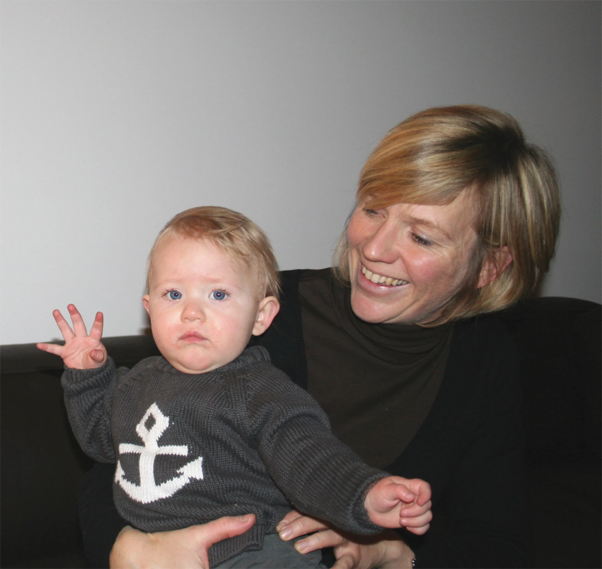 Lächelnde Frau hält ein Baby in einem Innenraum mit neutralem Hintergrund