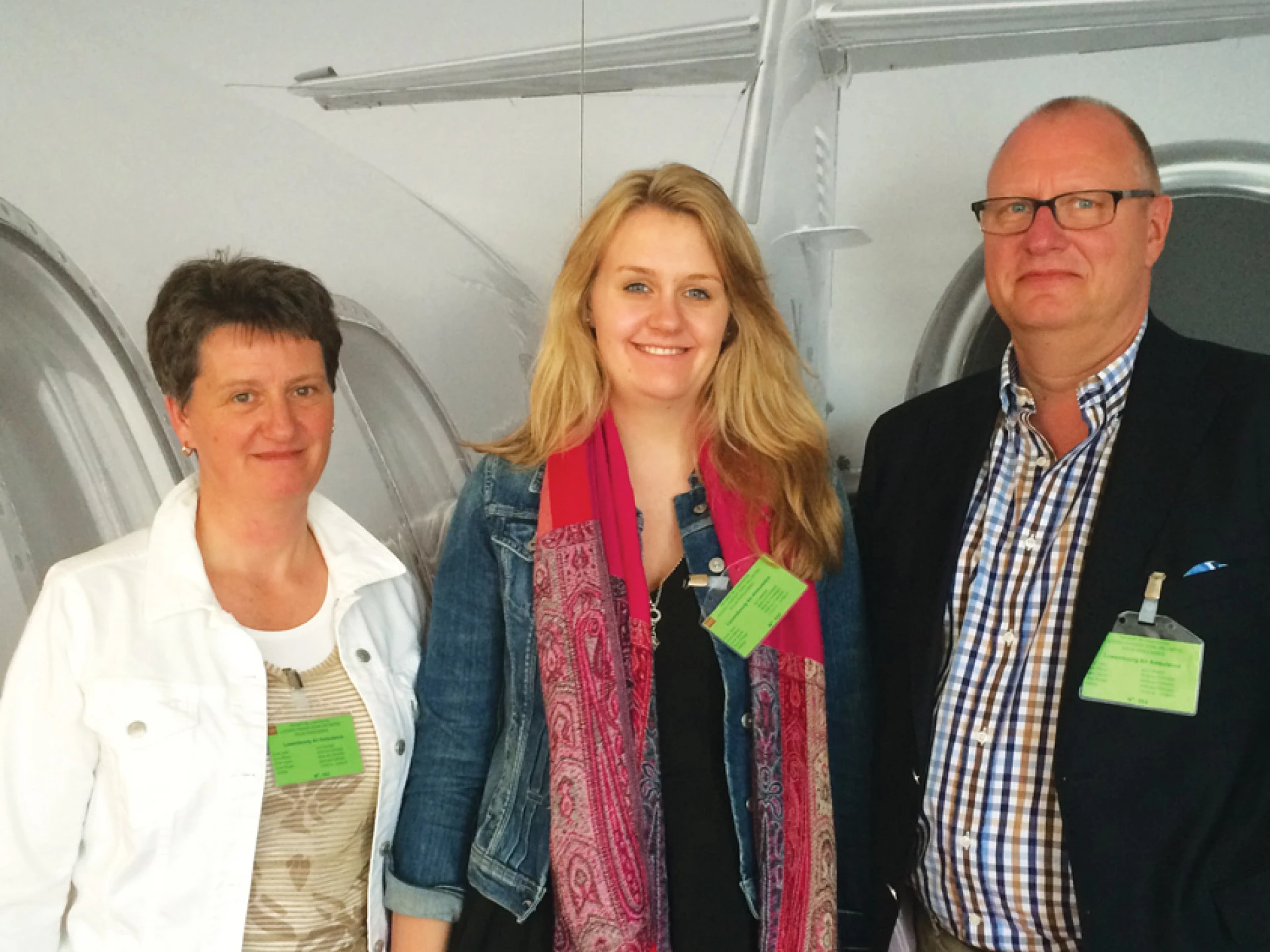Three adults standing indoors wearing visitor badges