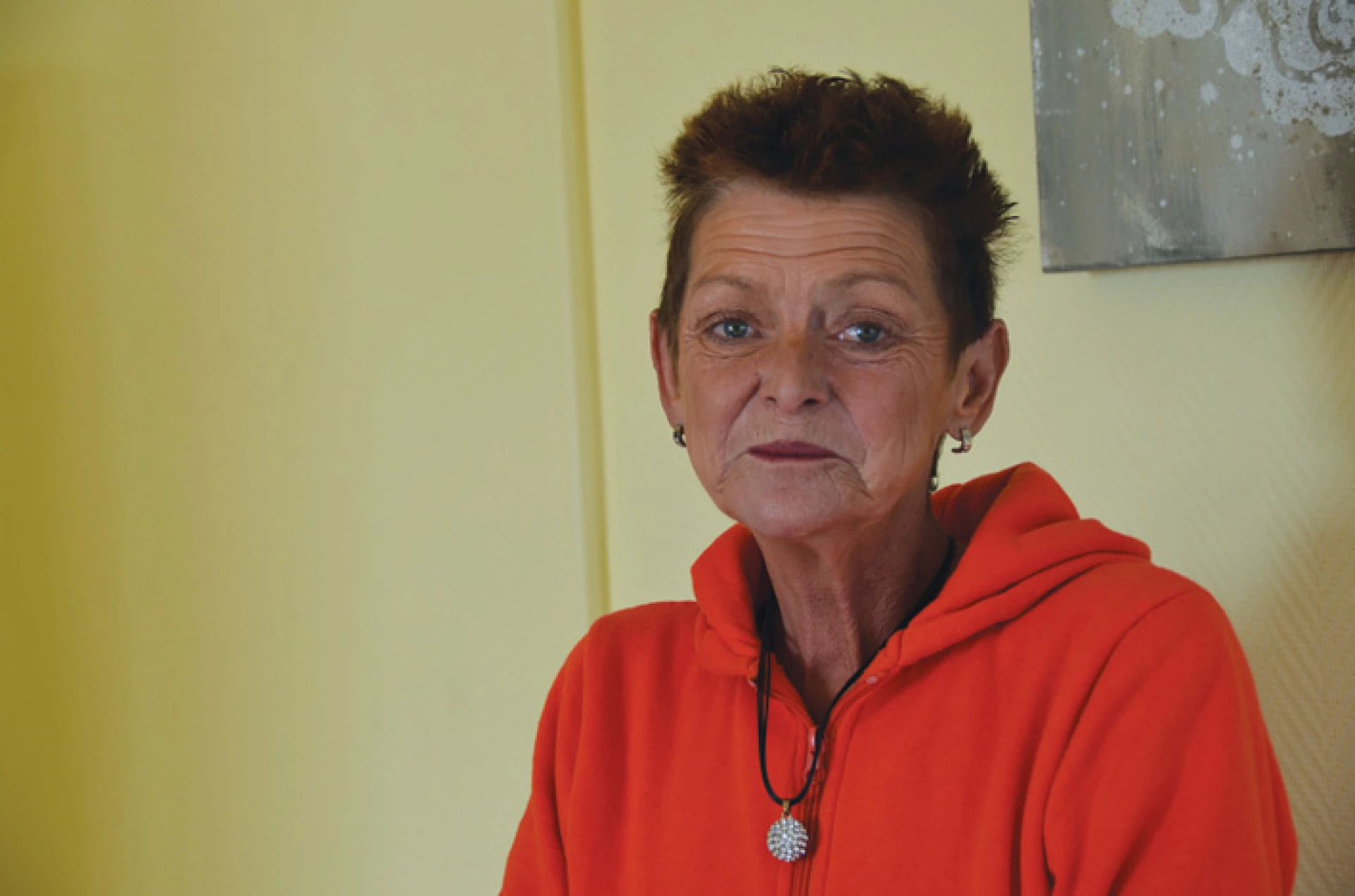 Portrait of an older woman indoors wearing an orange hoodie