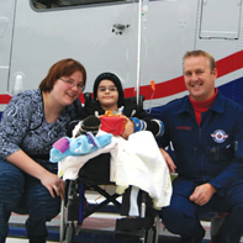 Kind im Rollstuhl mit Erwachsenen neben einem medizinischen Transportfahrzeug