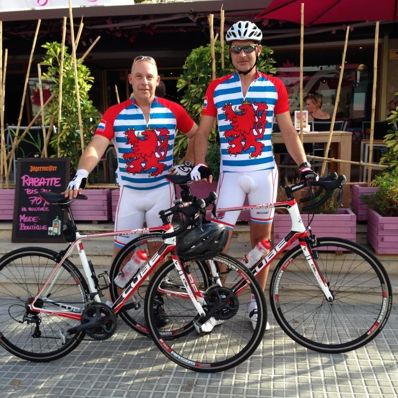 Two cyclists standing with road bikes in front of a café wearing matching jerseys.
