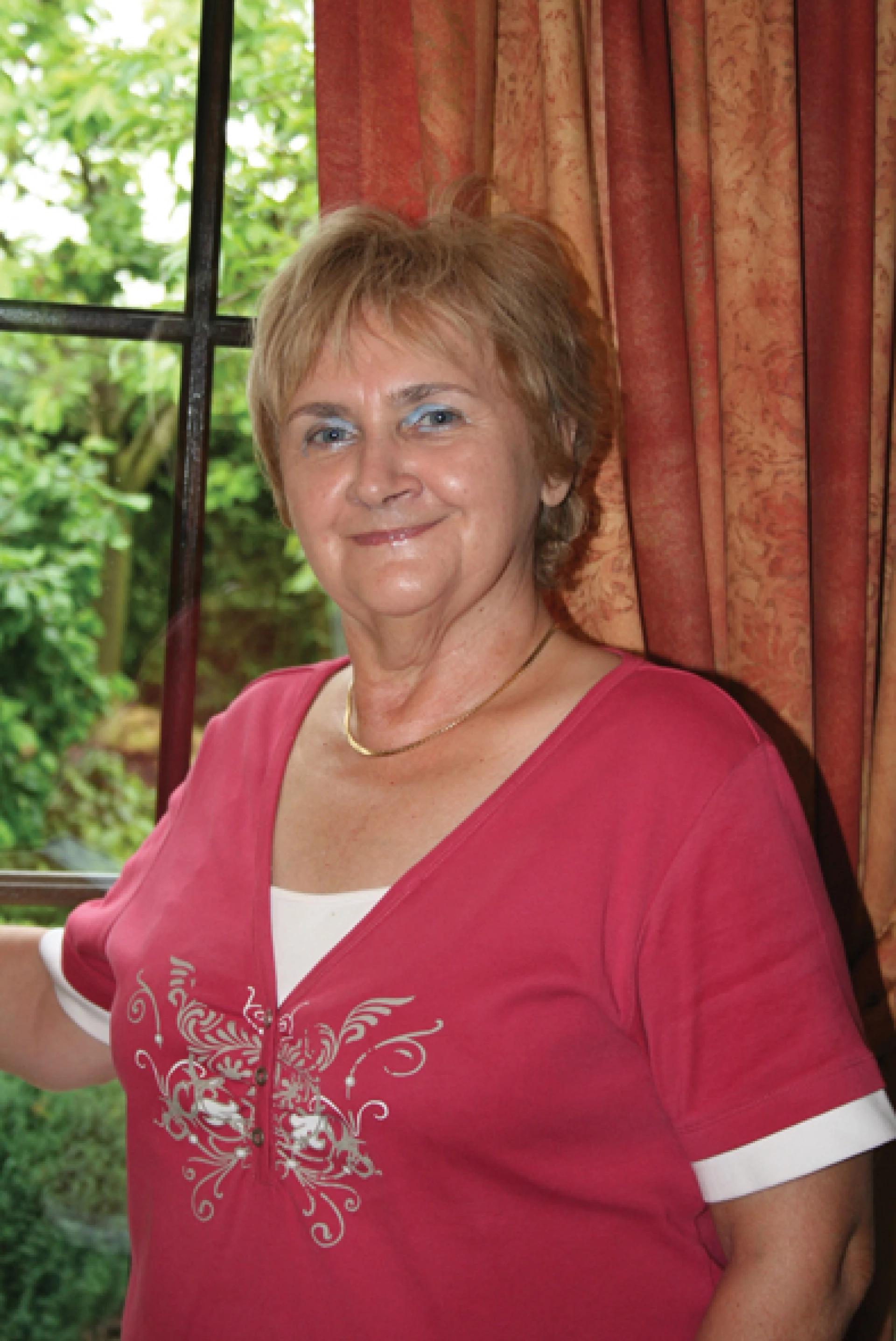 Lächelnde ältere Frau steht nahe einem Fenster mit Tageslicht