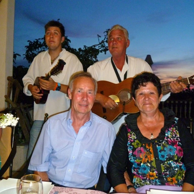 Group of adults enjoying dinner while musicians play live music in the background.
