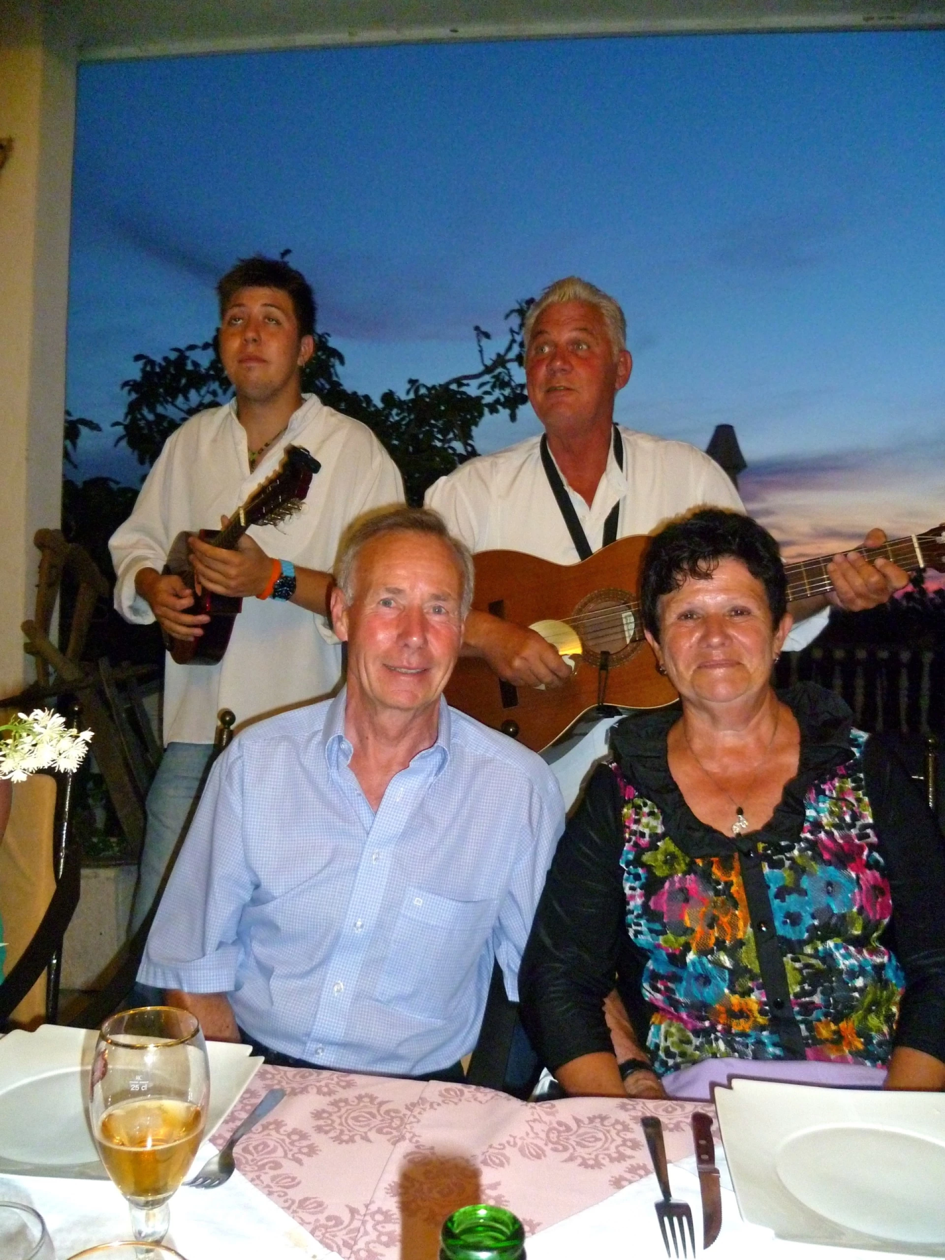Group of adults enjoying dinner while musicians play live music in the background.
