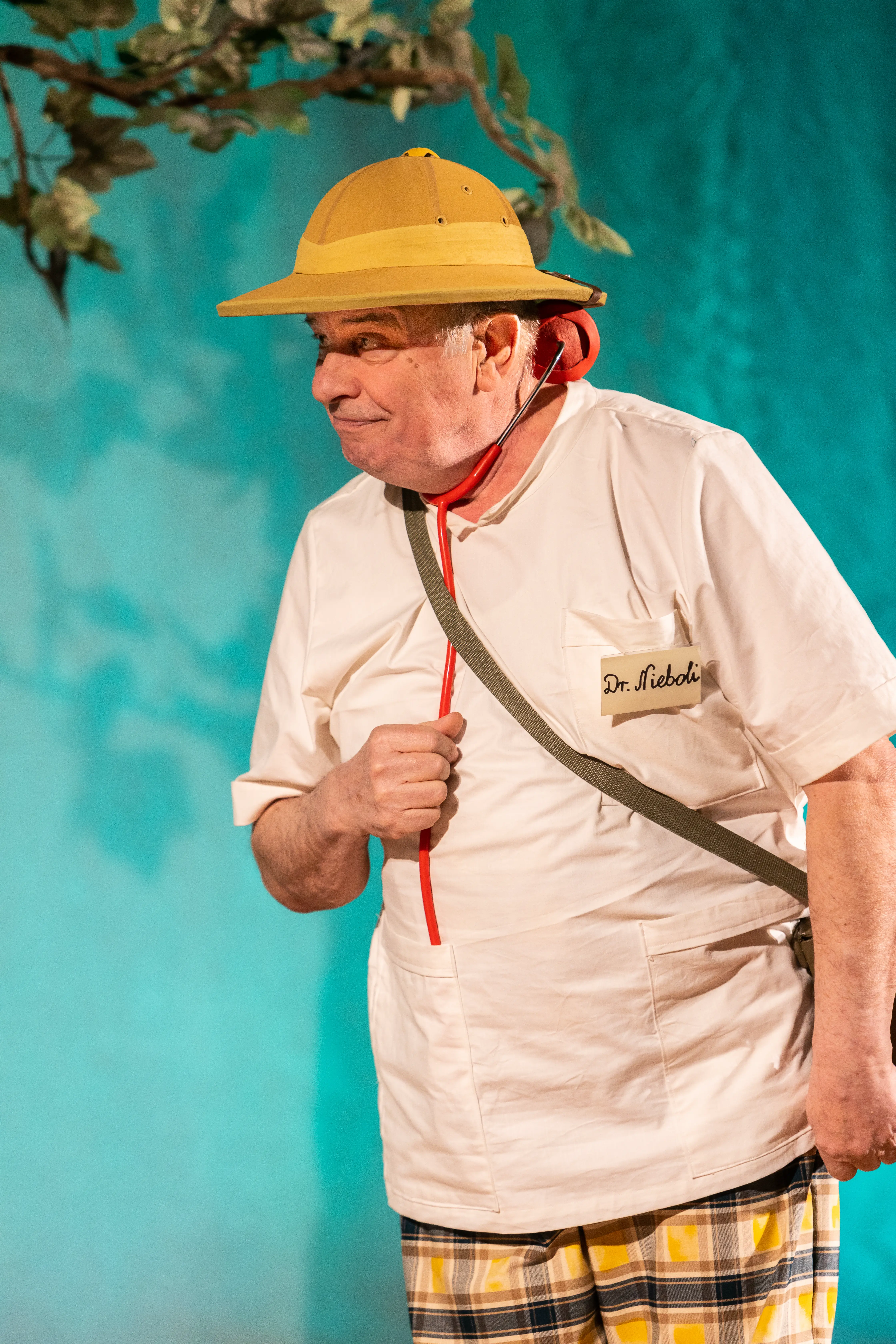 Spektakl – aktor w kapeluszu – Aktor w beżowym kostiumie i kapeluszu gra na scenie teatralnej.