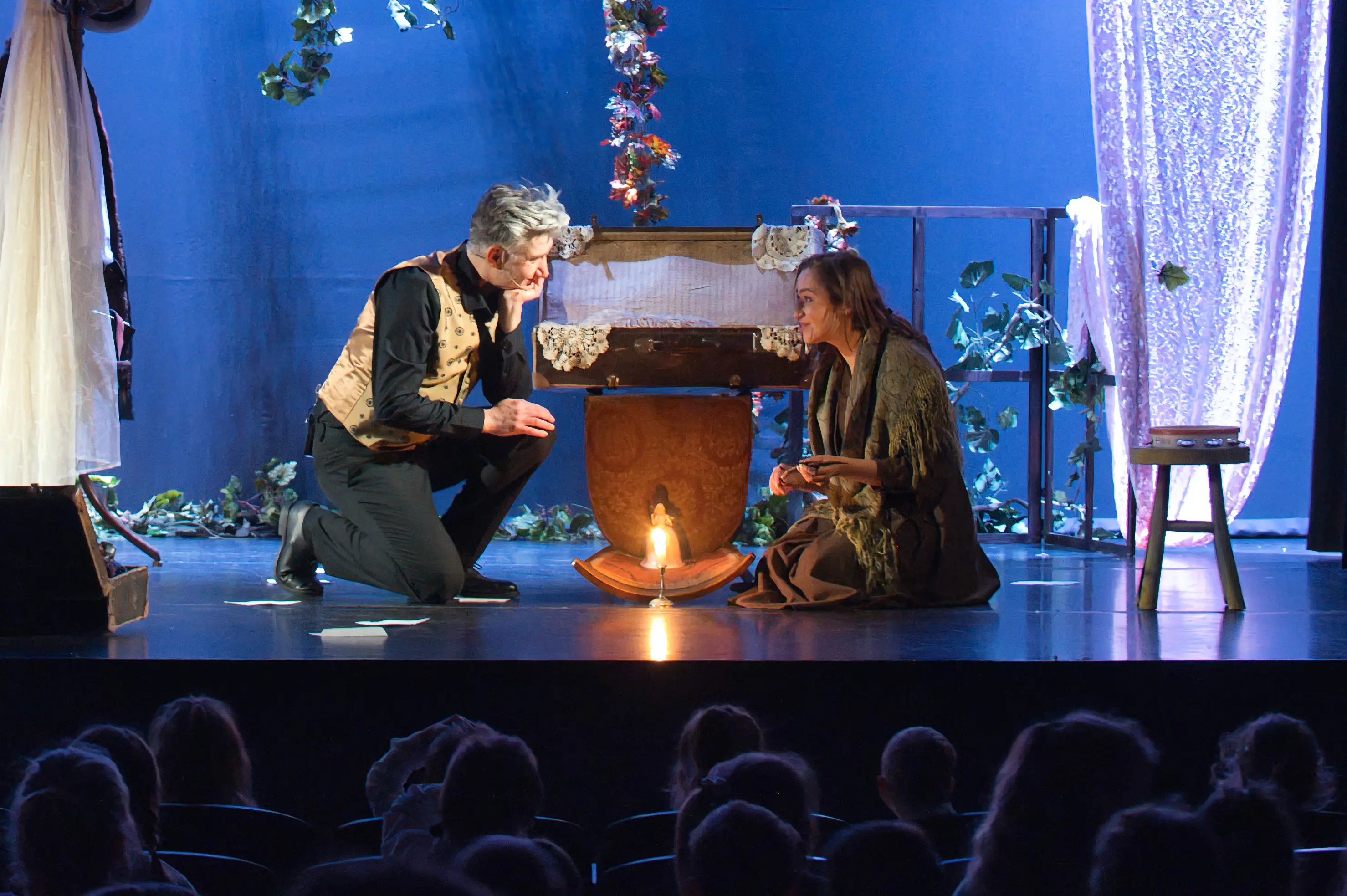 Spektakl z aktorem przy stole – Mężczyzna siedzi przy stole na tle dekoracji przypominającej pokój.