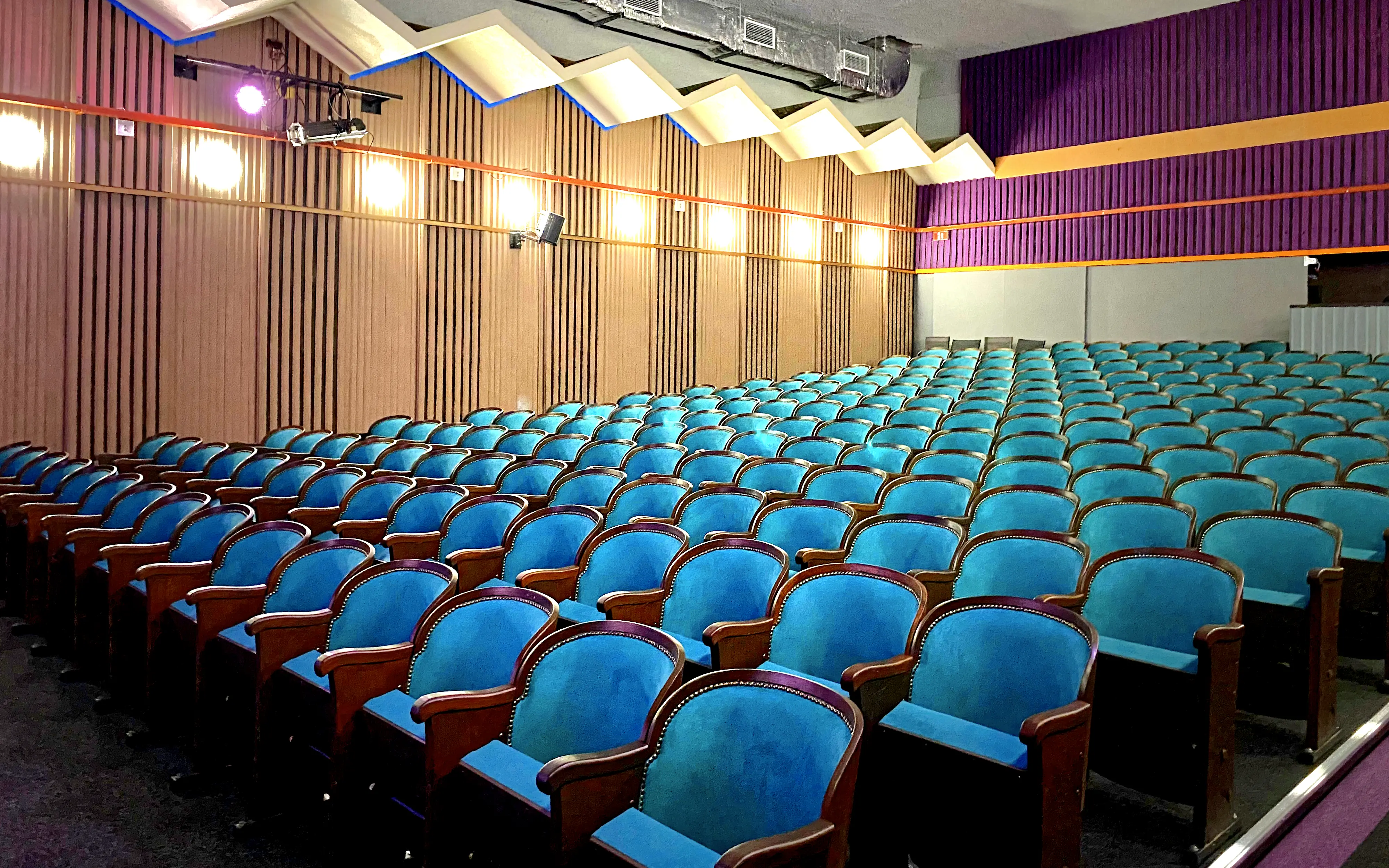 Sala teatralna – Widok wnętrza sali teatralnej z rzędami niebieskich foteli i sceną z zasłonami.