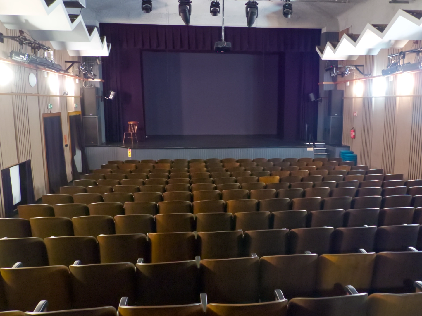 Sala teatralna – Widok wnętrza sali teatralnej z rzędami foteli i sceną z zasłonami.
