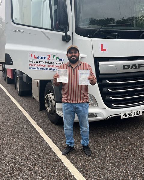 Hamza with a Class 1 pass certificate in front of a Learn2Pass training lorry