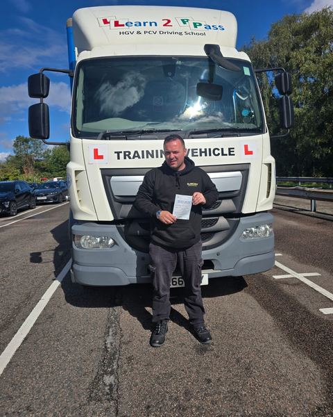 Daniel with a Class 2 pass certificate in front of a Learn2Pass training lorry