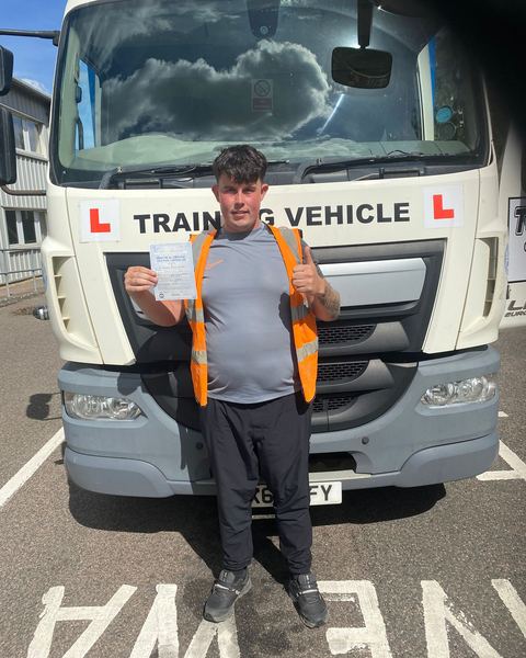 Brandon with a Class 2 pass certificate in front of a Learn2Pass training lorry