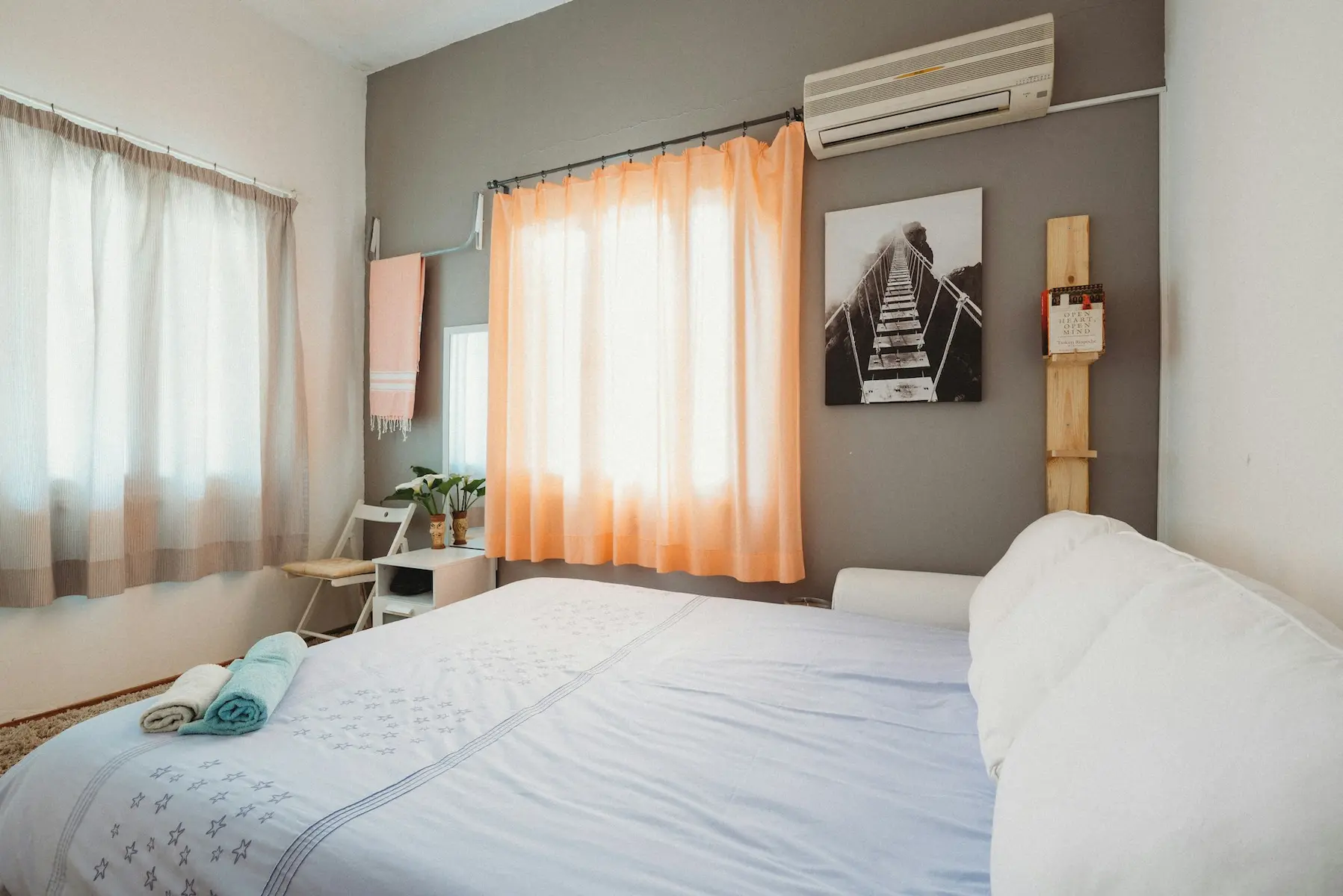Bright and cozy Airbnb bedroom with double bed, soft peach curtains, air conditioning, wall art, and neatly folded towels for guests.