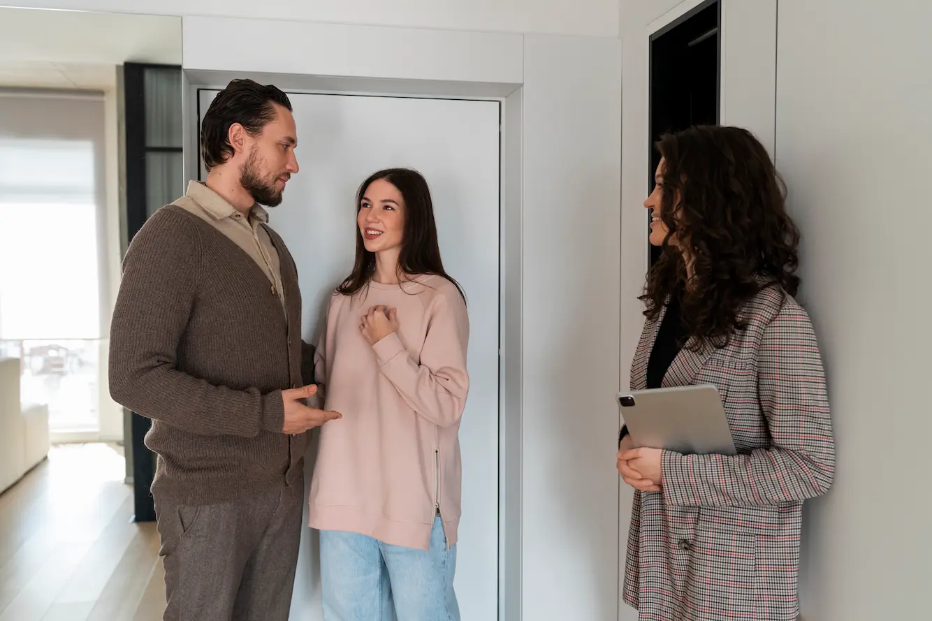A property manager welcoming a couple of guests and showing them around a short-term rental apartment, illustrating personalized hospitality supported by digital tools.
