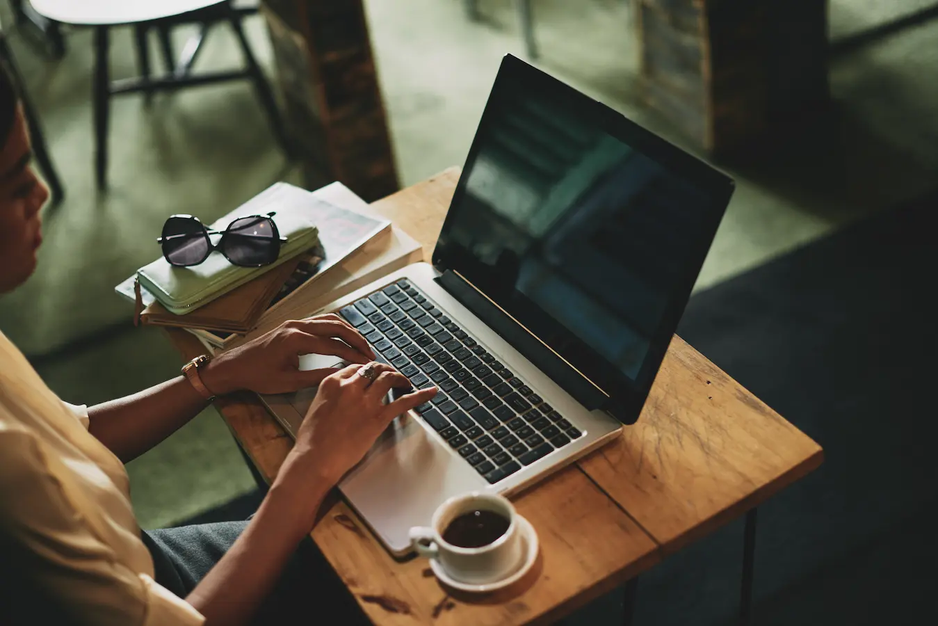 Person creating a digital welcome guide on a laptop, seated at a table with a cup of coffee.