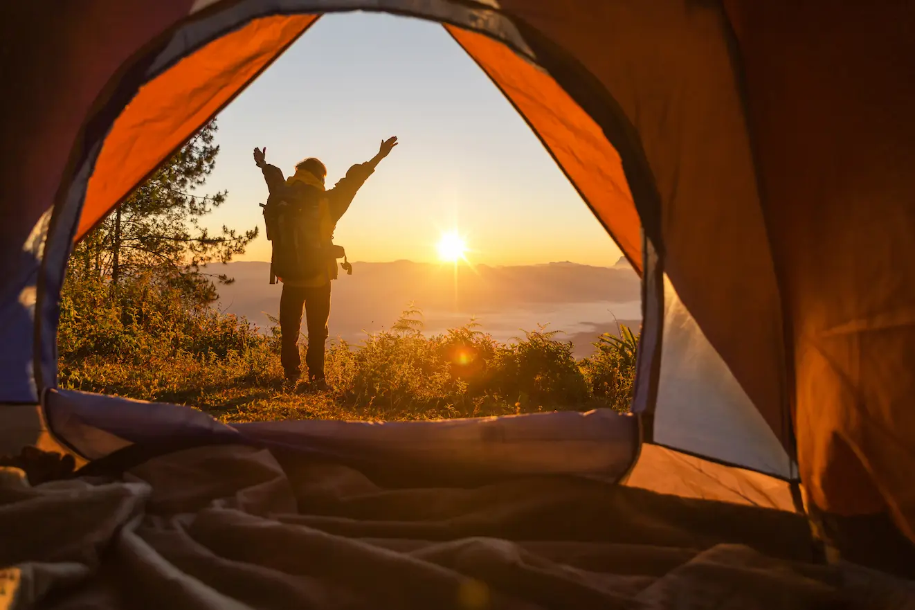 Vacancier profitant d’un lever de soleil devant sa tente dans un camping en pleine nature.