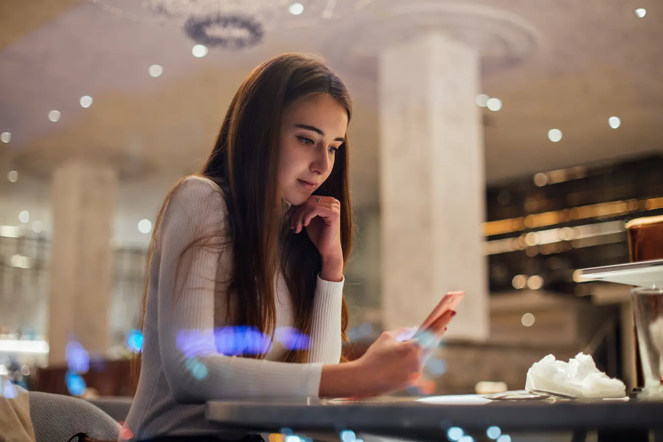 hotel guest seated in a dimly lit, modern luxury lounge, using her smartphone to interact with AI-powered digital welcome guide