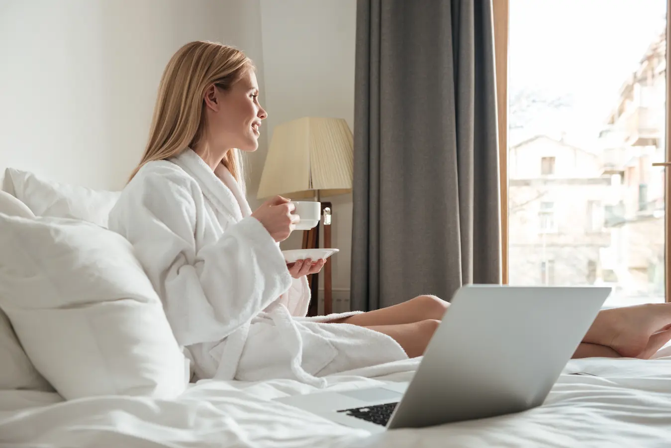 client d’hôtel détendu dans son lit avec un ordinateur portable et un café, profitant d’une expérience digitale fluide