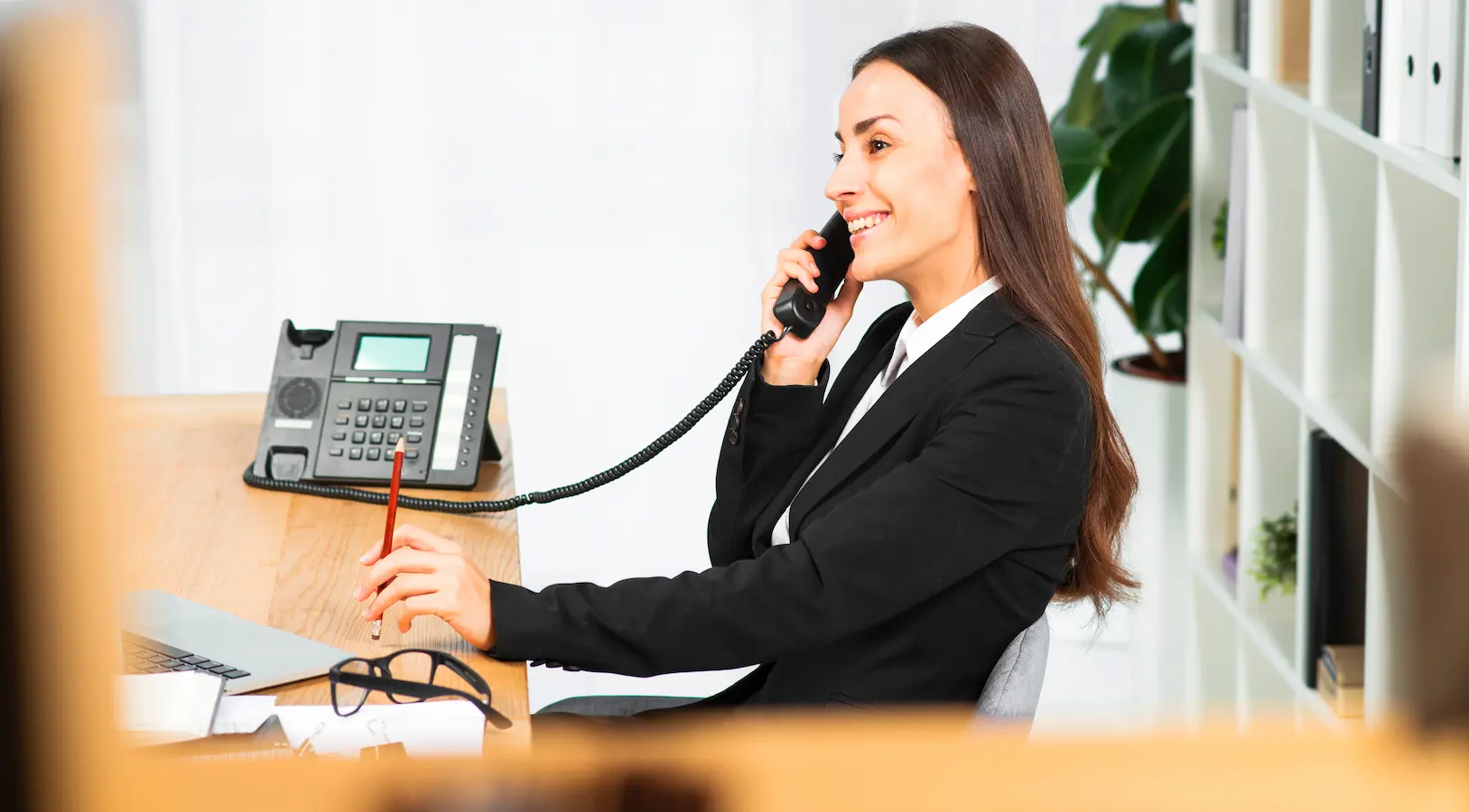 Hotel receptionist answering a phone call at the front desk while working on a computer.