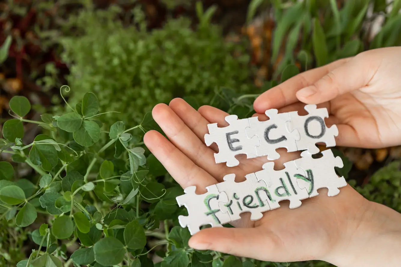 Hands holding puzzle pieces with the words “eco friendly” in front of green plants, symbolizing sustainability and environmental responsibility.