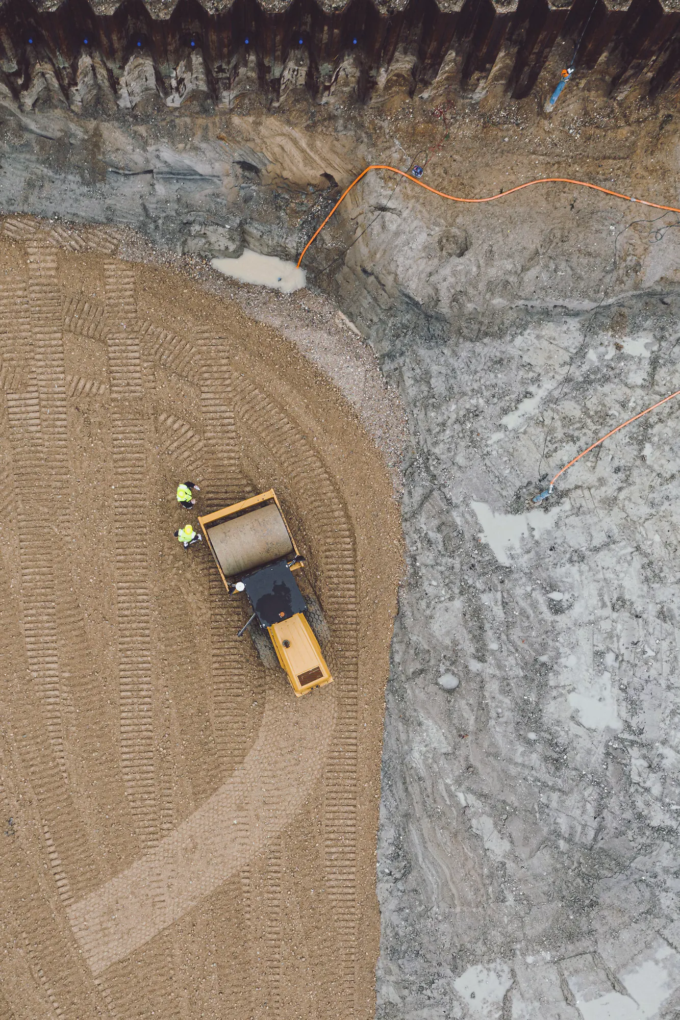 Compactor and workers on a construction site, seen from above