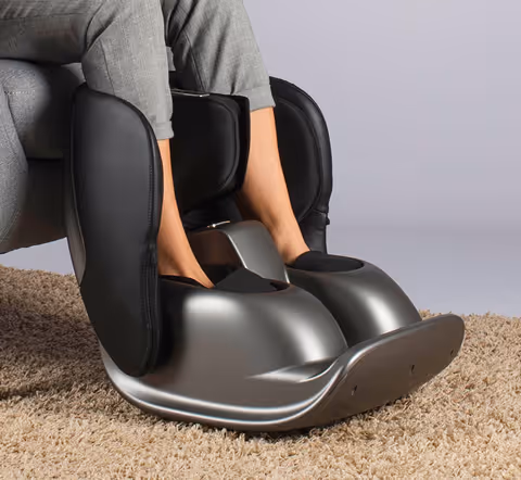 Personne utilisant un masseur de pieds noir Pedimass et argenté placé sur un tapis beige.