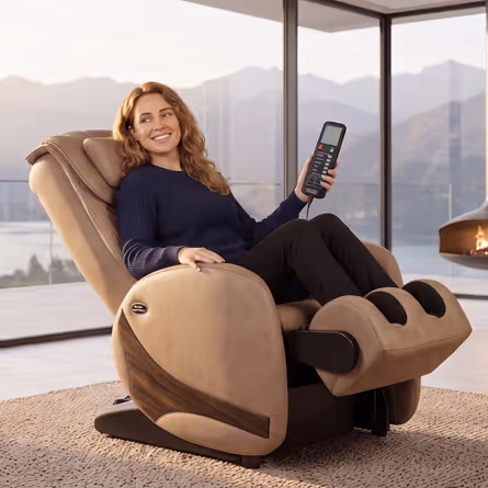 Femme souriante assise dans un fauteuil de massage Kin Relax beige avec télécommande, vue sur des montagnes à travers une baie vitrée.