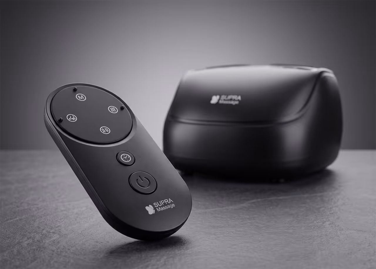 Télécommande avec logo Supra Massage posée devant l'appareil de massage Pédirelax sur surface grise.