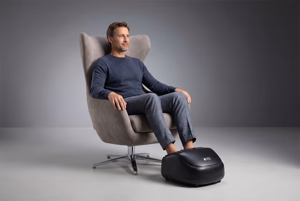 Homme assis sur un fauteuil gris utilisant l'appareil de massage Pédirelax pour les pieds.